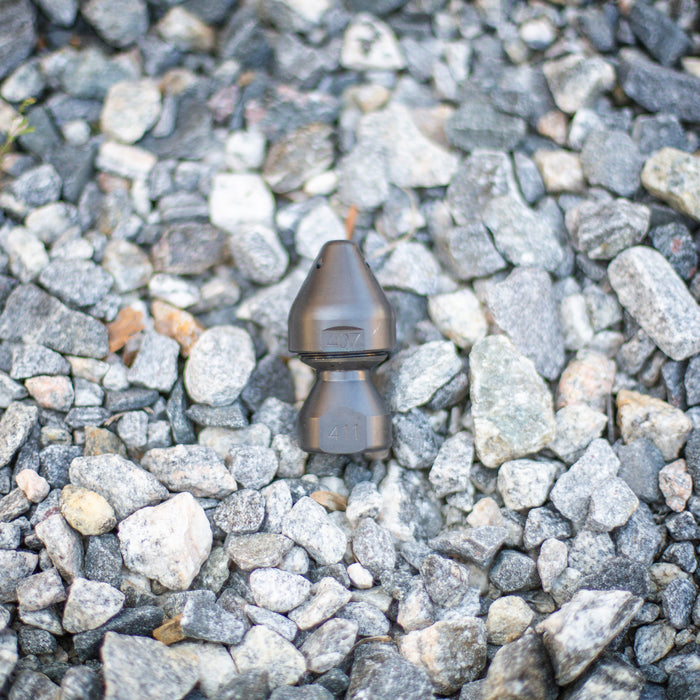 US Jetting RPD Egghead Penetrator nozzle made of case‑hardened steel, shown on gravel with engraved 407 and 411 markings, featuring a rounded nose and two‑piece removable cap for easy cleaning; high‑pressure sewer jetting nozzle engineered with forward and rear jets for cutting through blockages, heavy grease, and root masses, compatible with 1/2", 3/4", and 1" hoses and rated for 14–65 GPM at 2,000–10,000 PSI.