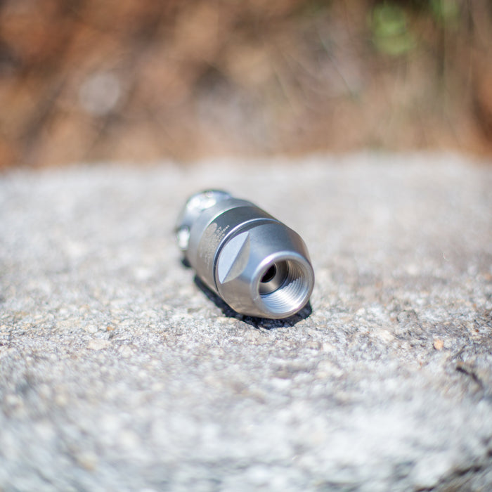 ENZ Bulldog rotating sewer jetting nozzle resting on a stone surface, featuring a stainless steel precision‑machined body with threaded inlet; built with an oil‑free braking system for controlled slow rotation and compatible with fresh or recycled water; engineered for cutting grease, roots, and heavy pipeline deposits using powerful 6-inch rear jets and a 1-inch forward jet, with optional 90‑degree descaling head available for removing tough scale from pipe walls.