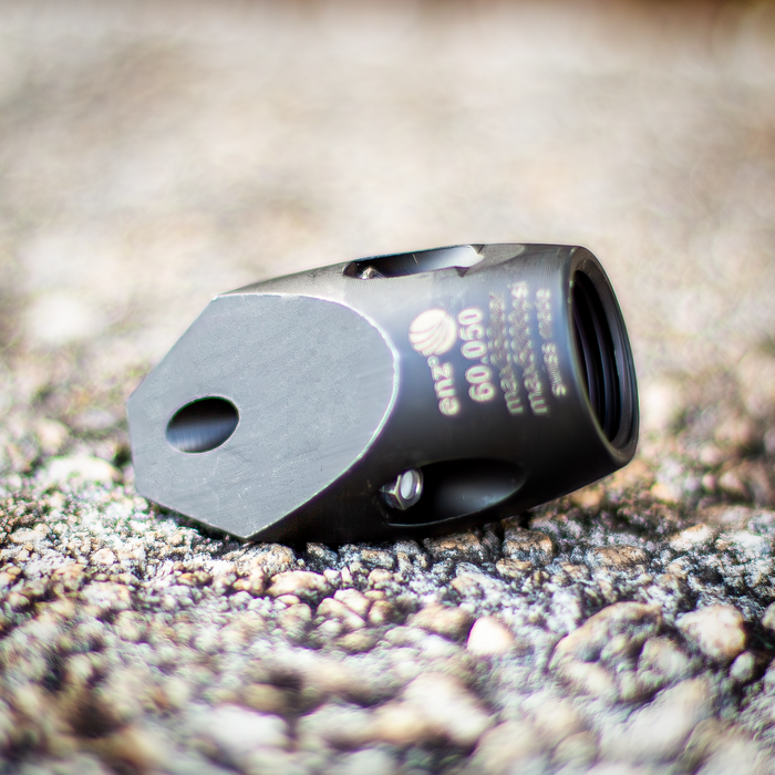 Enz 60.050 replacement chisel‑nozzle component shown in close‑up on a textured outdoor surface, featuring a black precision‑machined body with internal threading and engraved torque and pressure specifications. Industrial sewer jetting part engineered for high‑pressure drain cleaning systems, designed to support forward‑cutting and rear‑thrust jet configurations for clearing grease, light roots, and general pipe debris.