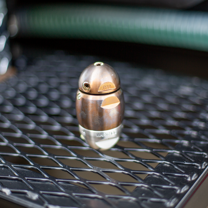 Warthog R22 high‑pressure sewer jetter nozzle on a black metal grate, featuring a two‑tone stainless steel and brass body with precision jet ports engineered for powerful pulling, descaling, and cleaning 3–8 inch sewer and drain lines. Durable, fully rebuildable design built for professional pipeline maintenance and heavy‑duty drain cleaning applications.