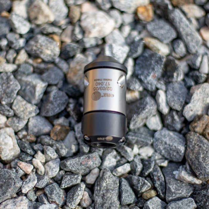 HRV Nozzle Swiss‑made precision metal component with engraved identifiers, cylindrical body and tapered tip, resting on gray industrial stones; high‑quality mechanical fitting used in professional engineering and manufacturing applications.