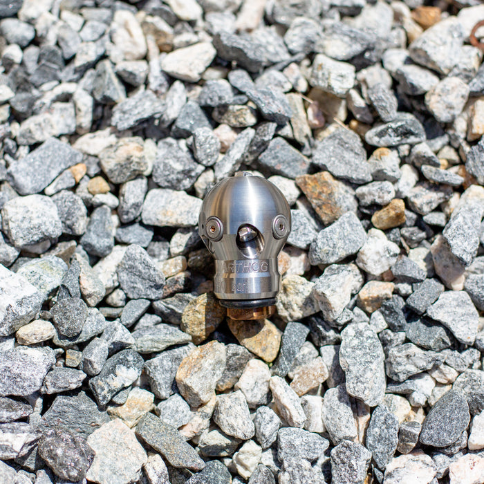 3/8" Warthog Mini Super Spin WT sewer jetting nozzle resting on gravel rocks, designed for 3–6 inch pipes and 3/8 inch hoses, ideal for grease, hair, and root removal, operating at 4000 PSI and 12 GPM, featuring 1 forward jet and 2 rear jets for strong propulsion and full orbital cleaning, controlled rotation ensures non-streak pipe wall cleaning and effective blockage penetration for residential and commercial drain applications.