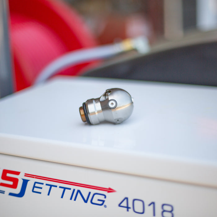 3/8" Warthog Mini Super Spin WT sewer jetting nozzle laying on its side atop a US Jetting 4018 jetter, designed for 3–6 inch pipes and 3/8 inch hoses, ideal for grease, hair, and root removal, operating at 4000 PSI and 12 GPM, featuring 1 forward jet and 2 rear jets for propulsion and full orbital cleaning, controlled rotation delivers non-streak pipe wall cleaning and effective blockage penetration for residential and commercial drain cleaning applications.