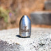 Reaper Rotating Nozzle placed on an outdoor concrete surface, featuring a polished stainless‑steel body with the engraved Reaper logo. This high‑pressure sewer jetting nozzle delivers a powerful forward oscillating jet and four rear propulsion jets to cut blockages, penetrate roots, and clear grease with a cone‑shaped spray pattern. Precision‑machined design ideal for professional drain cleaning, available in multiple pressure and flow sizes from US Jetting.