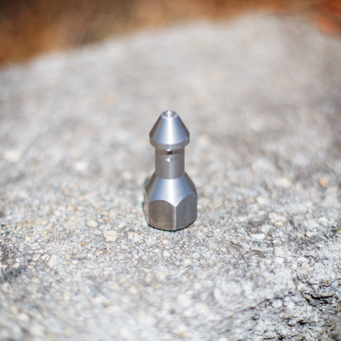 USJ Penetrator 1/2-inch stainless steel sewer jetting nozzle on a rough stone surface, close-up of precision-machined forward jet and six rear jet ports engineered to break through hard blockages like packed debris or ice; high‑pressure 4018 jetter nozzle with adapters available for other hose sizes.