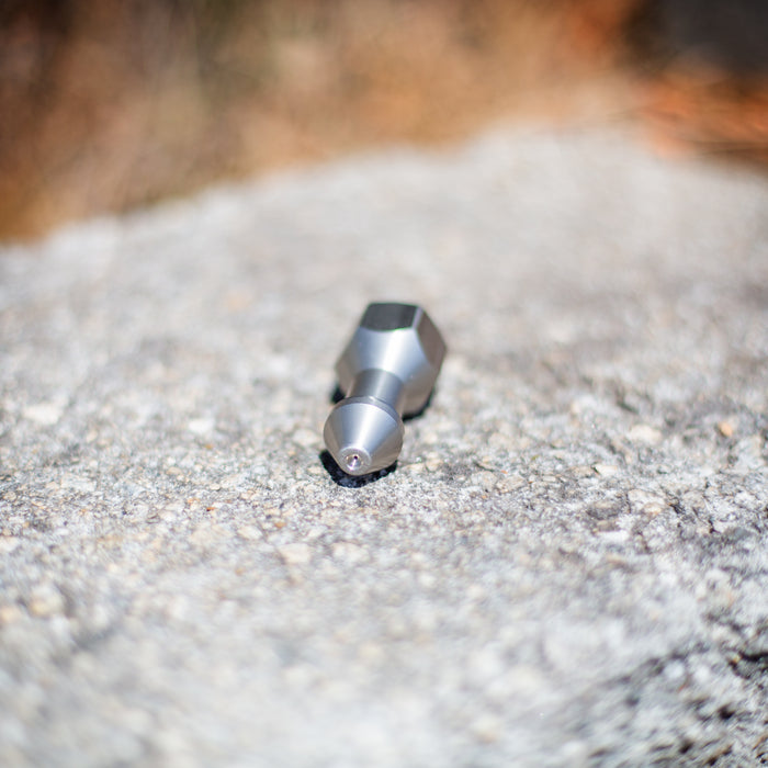 USJ Penetrator 1/2-inch stainless steel sewer jetting nozzle on rough stone surface, close-up of precision‑machined forward jet and six rear jet ports engineered to break through hard blockages like packed debris or ice; high‑pressure 4018 jetter nozzle with adapters available for other hose sizes.