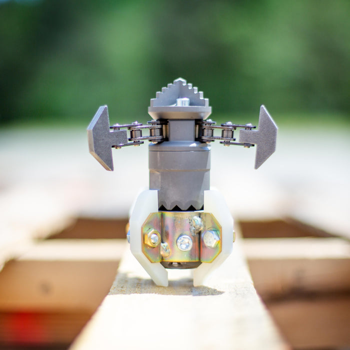 Close‑up of an ENZ Turbo Chain Scraper nozzle on a wooden pallet, featuring dual arrow‑shaped rotating chain arms, adjustable chain lengths, and white centralizing skids. Heavy‑duty sewer jetting tool engineered for removing concrete, roots, and grease from 3–8 inch pipes, built for rugged conditions and compatible with jetting machines requiring at least 8 GPM.